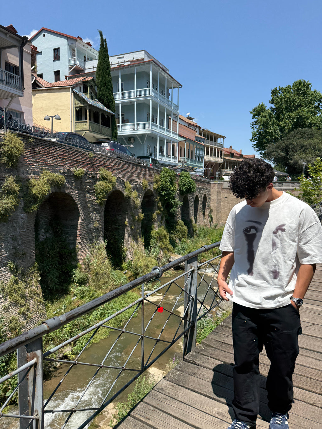 Person standing on a bridge overlooking a cityscape with buildings and greenery.