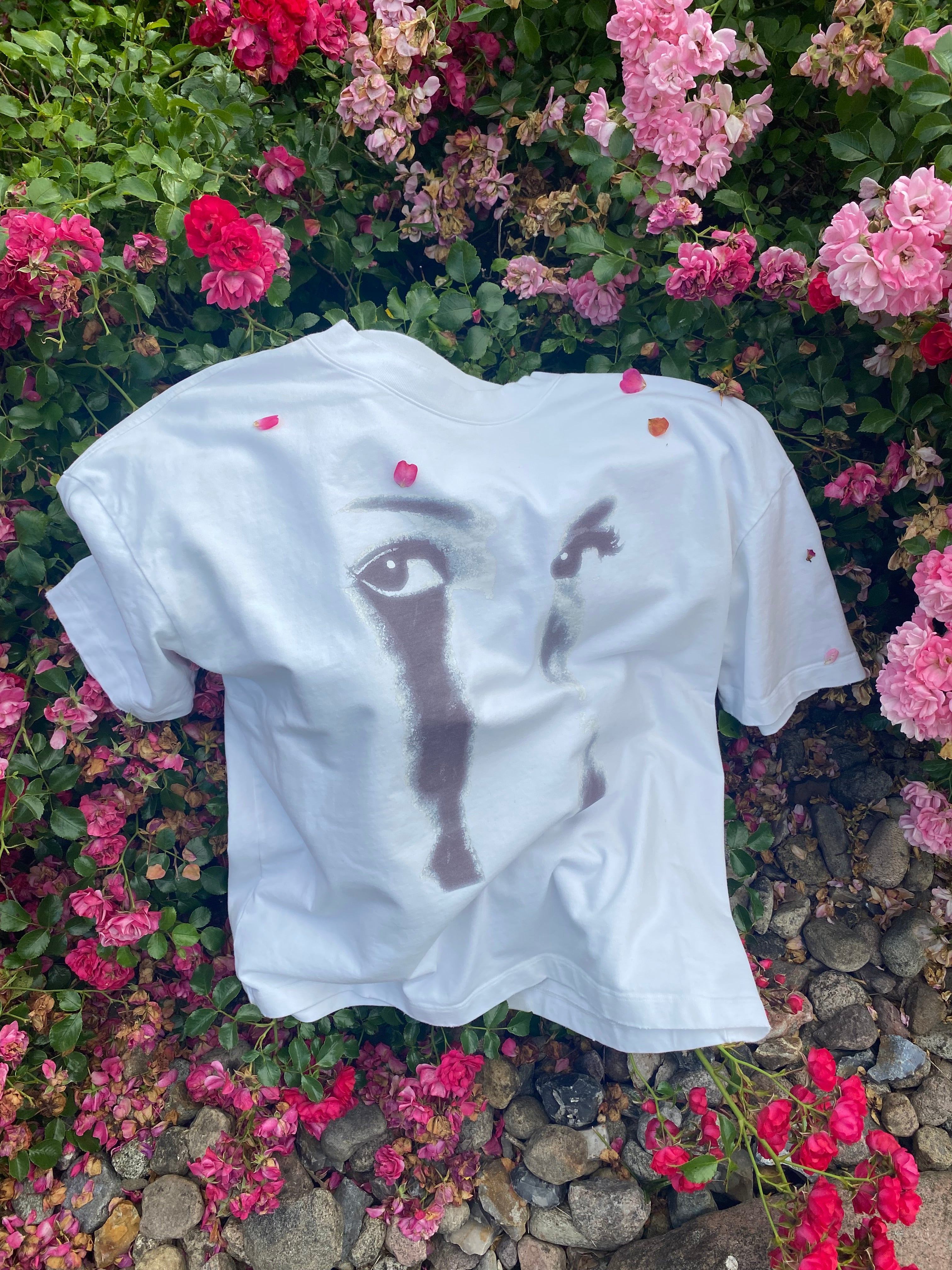 White t-shirt with black design on a bed of pink flowers and stones